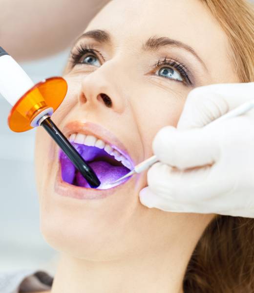 Close-up partial view of dentist using dental curing UV lamp on teeth of patient